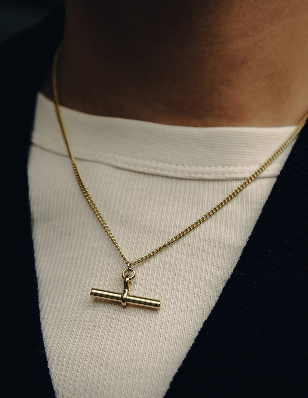 Gold necklace with a clasp on a person wearing a white shirt.