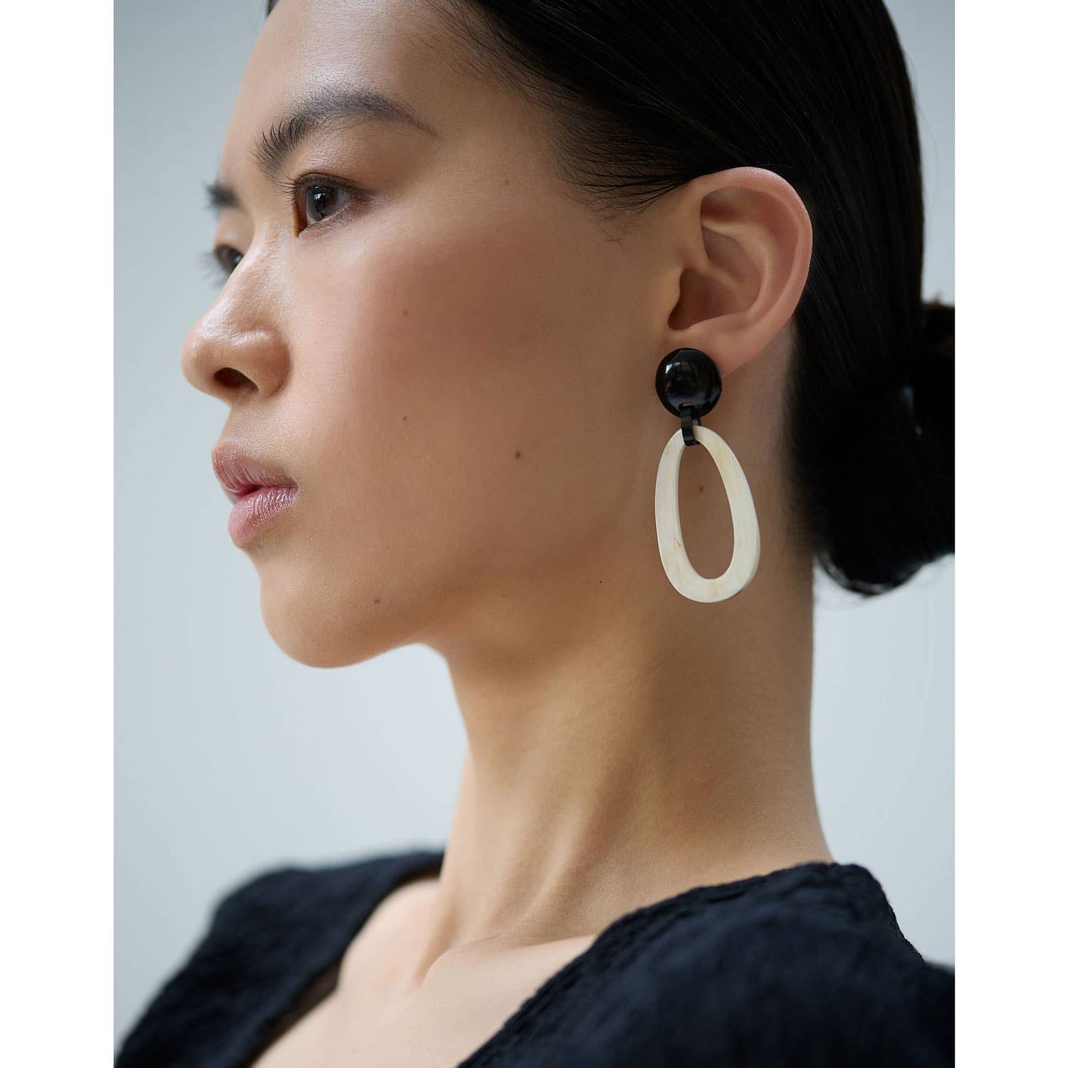 Woman wearing a black and white earring on a plain background